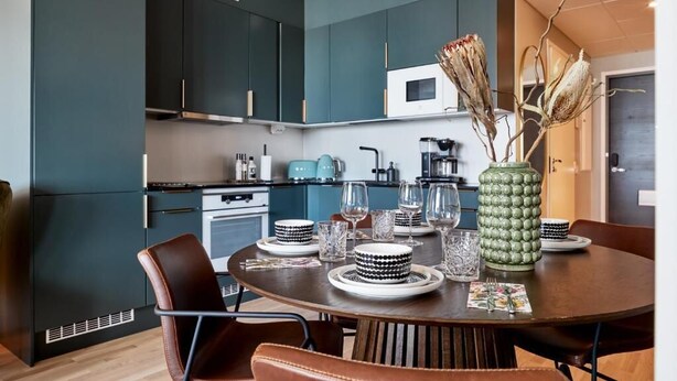 Una cocina moderna con armarios azul oscuro, un microondas y una zona de comedor con una mesa redonda para cuatro.