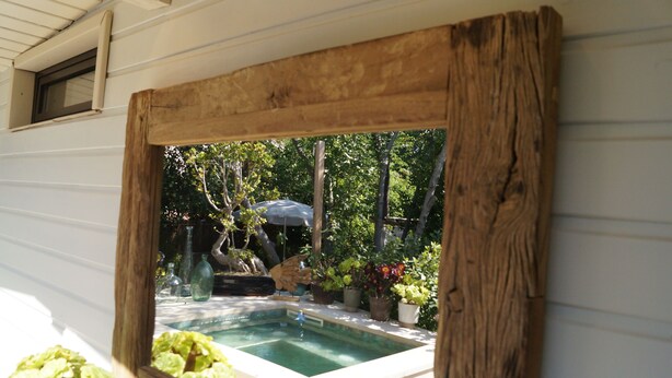 A wooden-framed window with a view of a swimming pool, potted plants, and a gazebo.