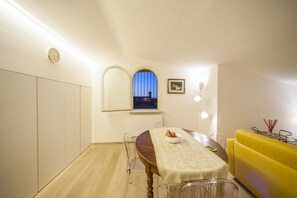 Ein Essbereich mit einem Holztisch, Stühlen, einem gelben Sofa, einer Uhr und einem Fenster mit Blick.