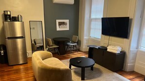 Uma sala de estar com sofá, mesa de centro, TV e um pequeno espaço de jantar.