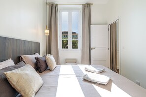 A hotel room with a bed, a window, a door, and a view of buildings outside. - Exceptional apartment in the heart of Nice (Nice)