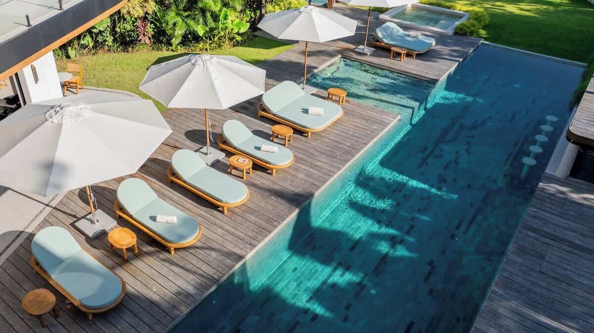 Un área junto a la piscina con sillones de descanso y sombrillas.