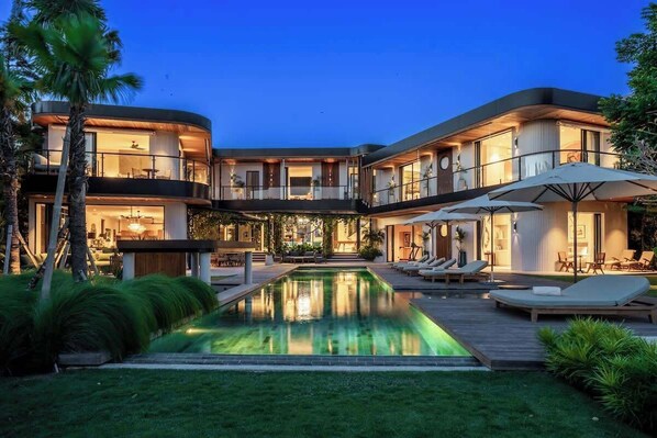 A modern multi-story building with a swimming pool, outdoor seating, and a well-maintained garden.