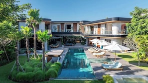 Une maison moderne à deux étages dotée d’une piscine, de chaises longues et d’un patio couvert.