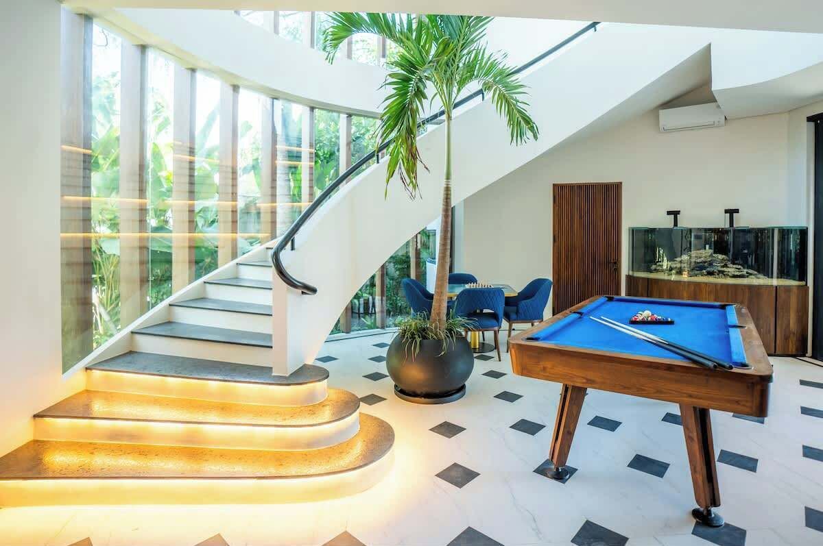 Een modern interieur met een pooltafel, een trap met verlichte treden en een groot raam met uitzicht op groen.