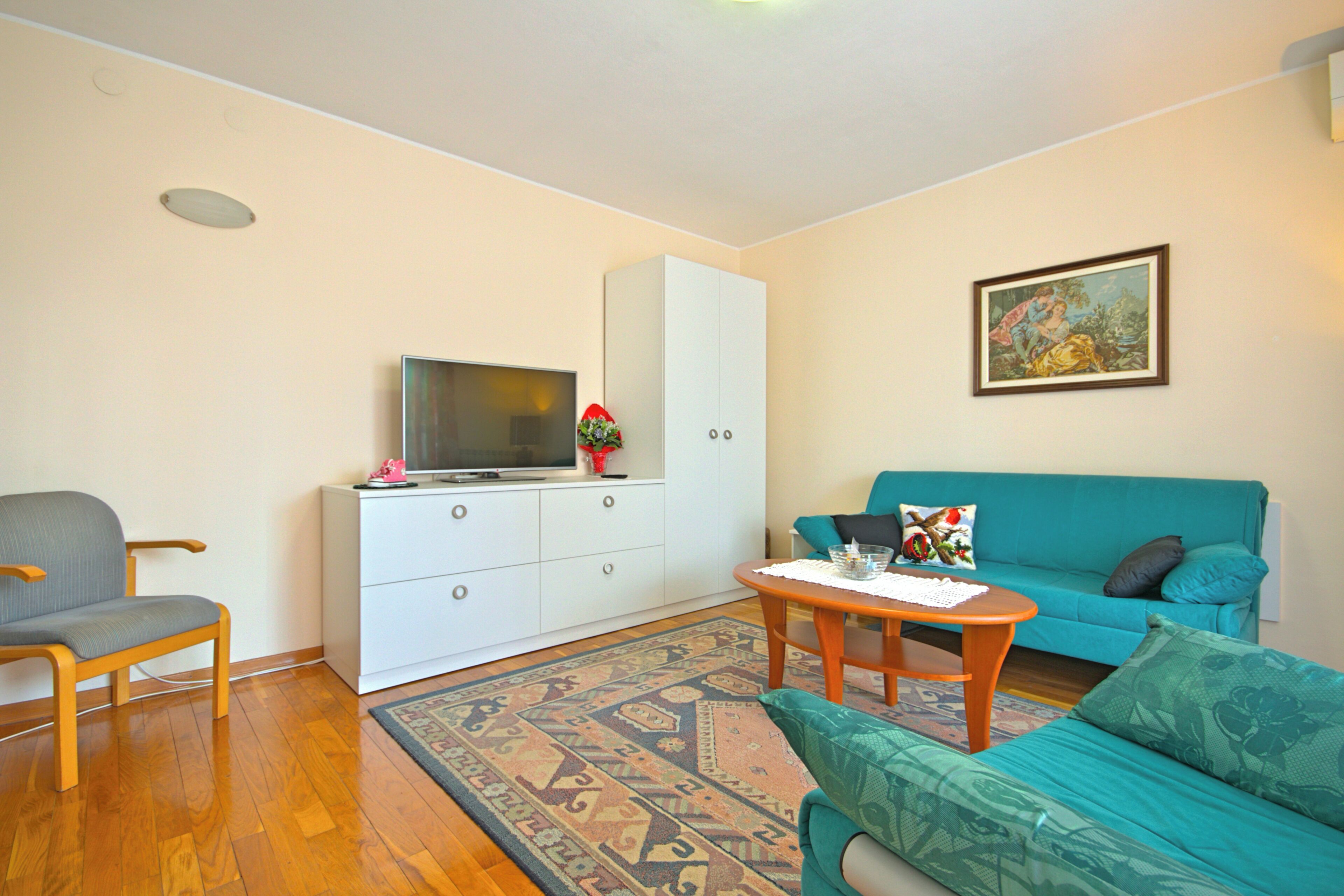 Un salon avec un canapé, un fauteuil, un téléviseur posé sur un meuble et un tableau accroché au mur.