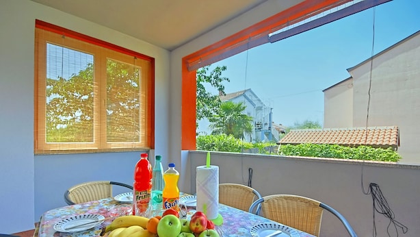 A balcony with a table set for dining, featuring a floral tablecloth, wicker chairs, and a fruit platter. - Coastal Serene Stay in Umag (Umag)