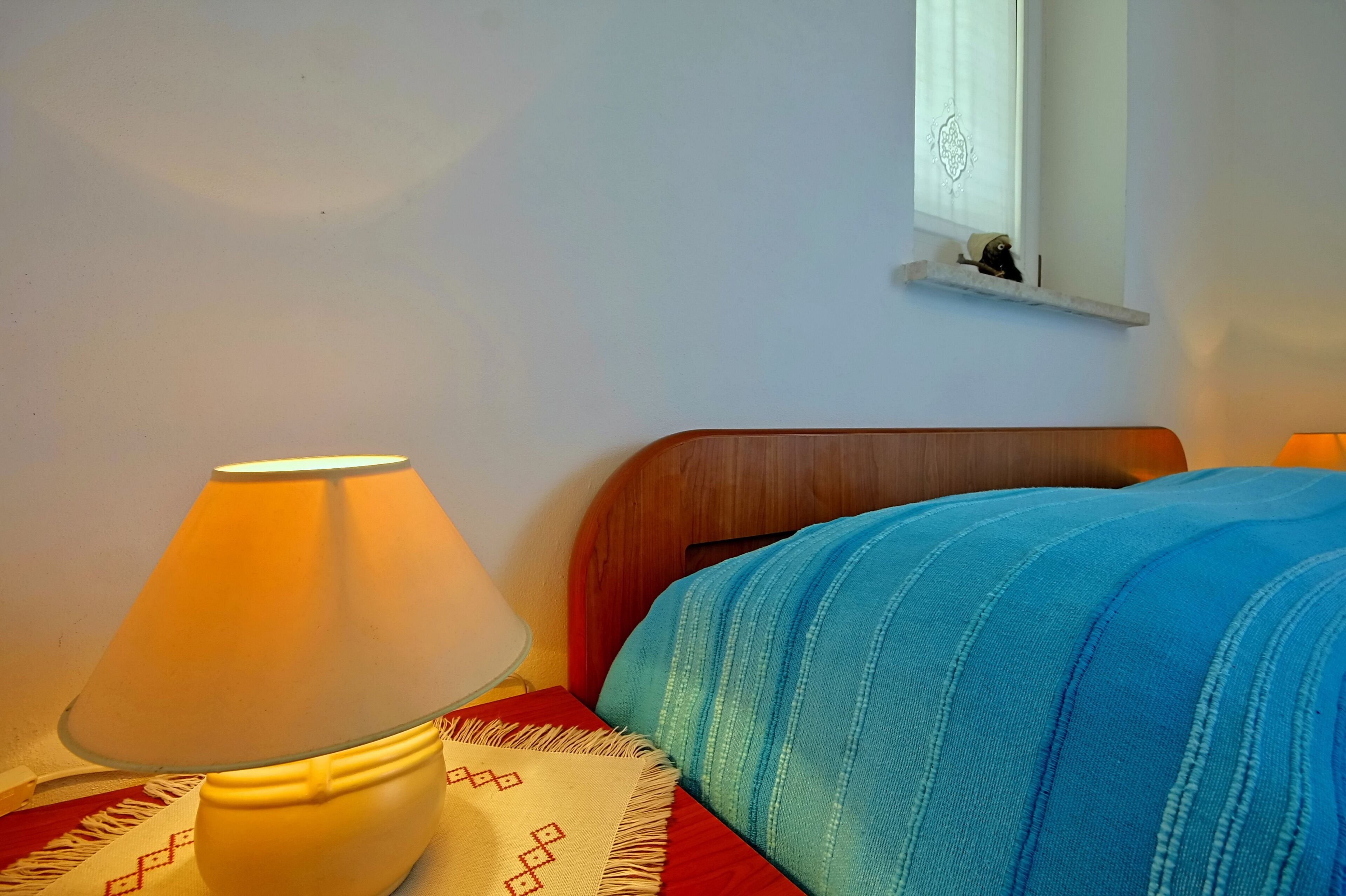 Un letto con testiera in legno, una lampada su un comodino e una finestra con tenda.