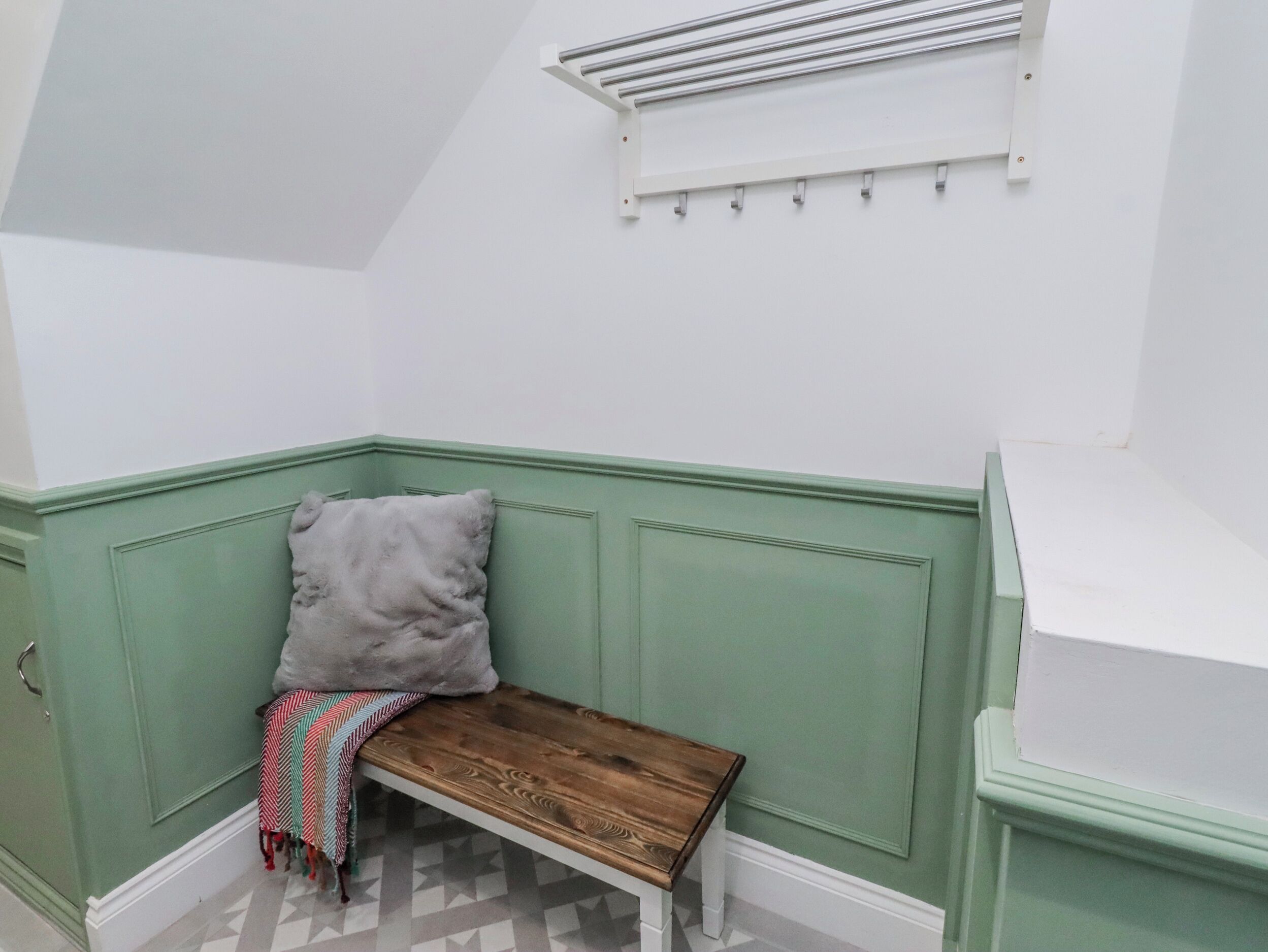 Une pièce d’angle avec un banc, un coussin, un radiateur et un sol à motifs.