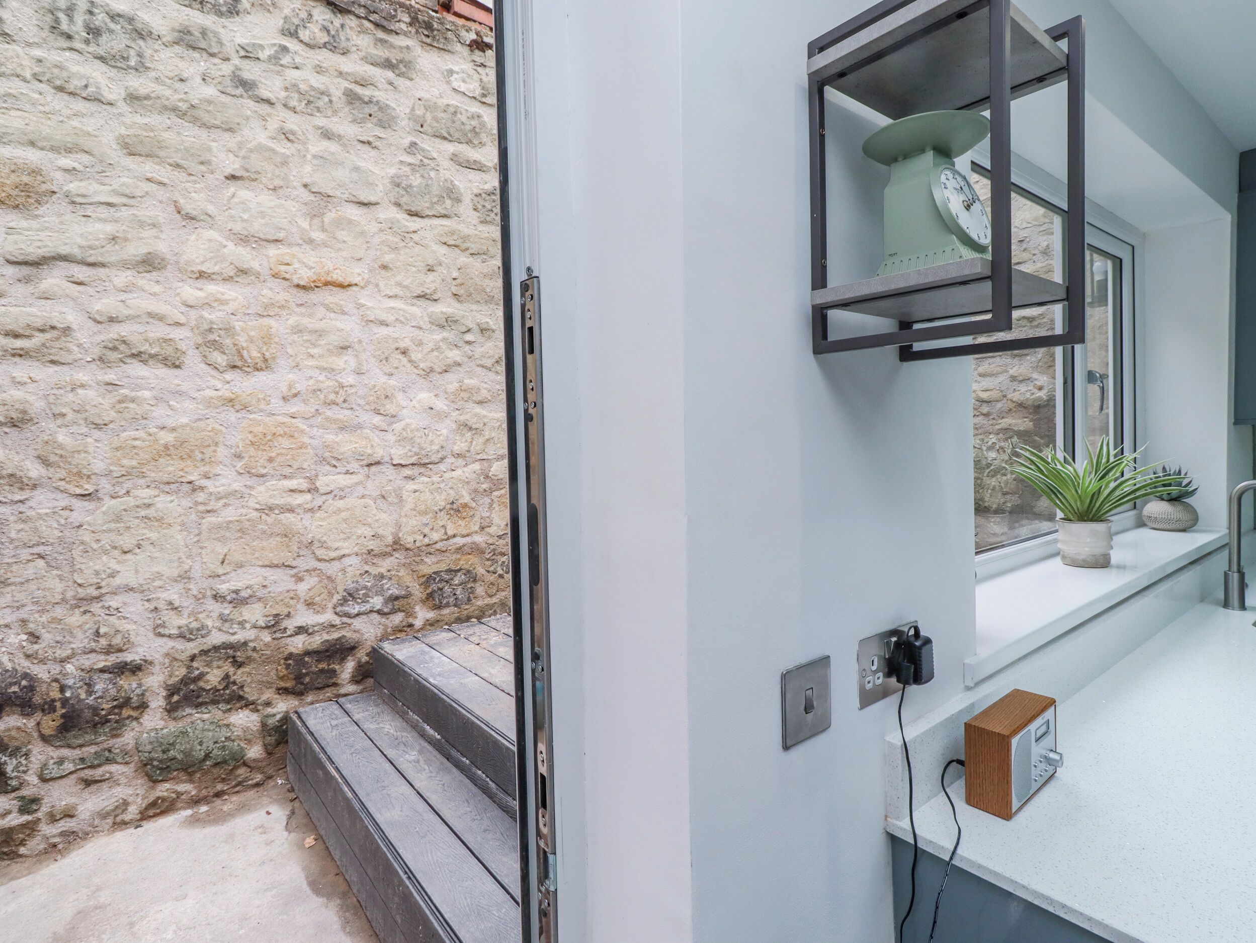 A bathroom with a stone wall, a sink with a mirror, a potted plant, and a wooden box.