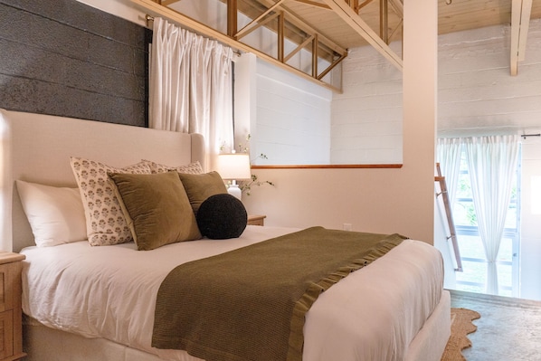 A bedroom with a bed, pillows, a lamp, and a window with curtains.