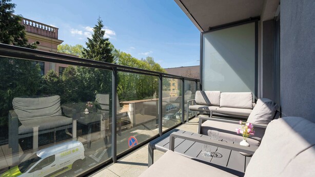 Un balcon doté d’une barrière en verre, d’un espace salon extérieur et offrant une vue sur la rue.
