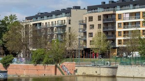 Un immeuble résidentiel à plusieurs étages, doté de balcons, avec une rivière au premier plan et une clôture verte.