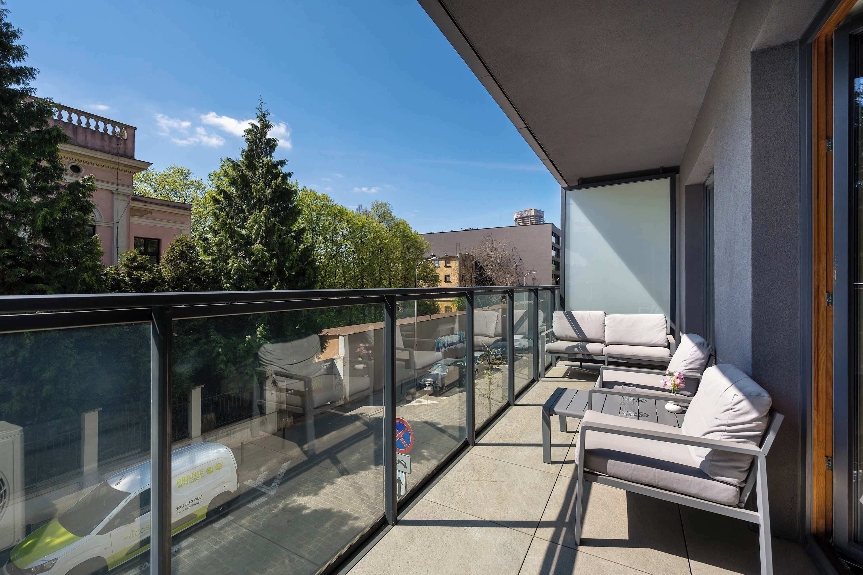 Ein Balkon mit Glasgeländer, Sitzmöglichkeiten im Freien und Blick auf eine Stadtlandschaft.