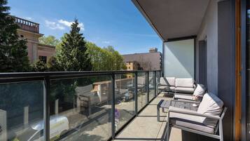 Ein Balkon mit Glasgeländer, Sitzmöglichkeiten im Freien und Blick auf eine Stadtlandschaft.