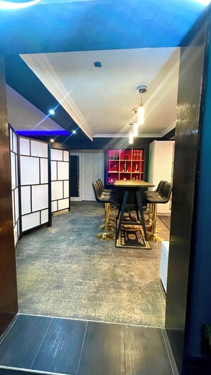 Un interior moderno con zona de comedor que incluye una mesa redonda y taburetes de bar, un estante decorativo con objetos y un papel tapiz estampado.