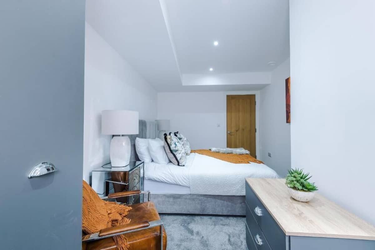A modern bedroom with a bed, bedside table, lamp, and a small potted plant.