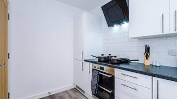 A modern kitchen with white cabinets, a black countertop, a microwave, an oven, and a tiled backsplash.