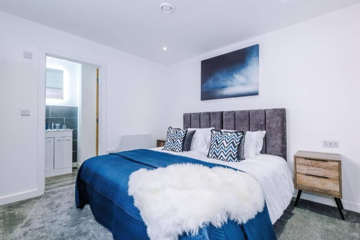 A bedroom with a bed, a nightstand, a wall-mounted artwork, and a door leading to a bathroom.