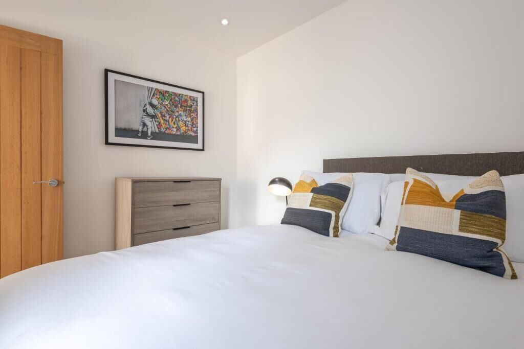 A bedroom with a bed, a wooden wardrobe, a nightstand, a lamp, and a framed picture on the wall.