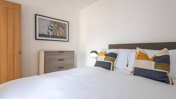 A bedroom with a bed, a wooden wardrobe, a nightstand, a lamp, and a framed picture on the wall.