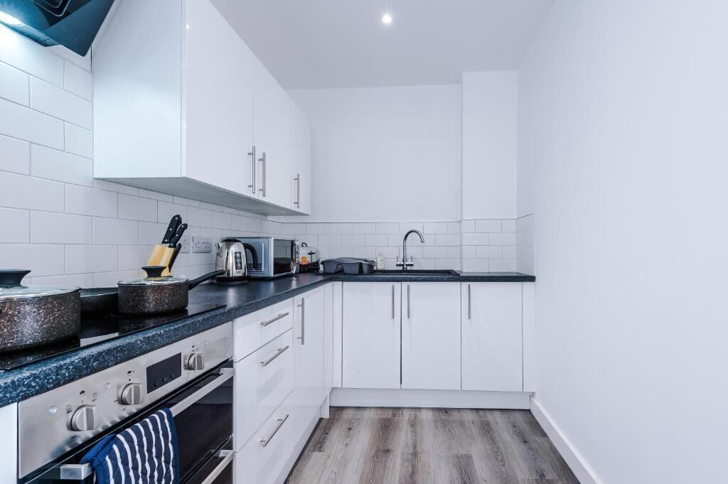 A compact kitchen with white cabinets, a black countertop, and a stainless steel range.