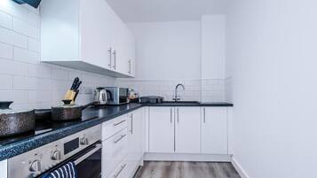 A compact kitchen with white cabinets, a black countertop, and a stainless steel range.