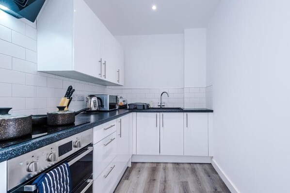A compact kitchen with white cabinets, a black countertop, and a stainless steel range.