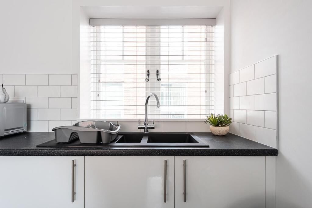 Een moderne keuken met een zwart aanrecht, een roestvrijstalen spoelbak en een raam met zonwering.