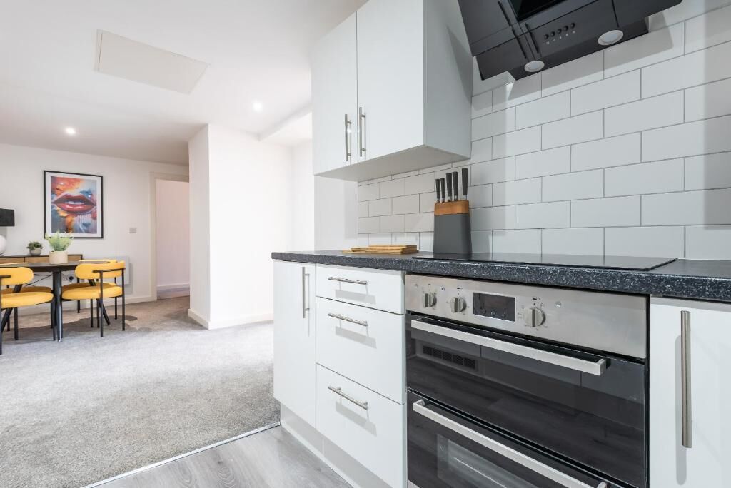 A modern kitchen with white cabinetry, black countertops, and stainless steel appliances.