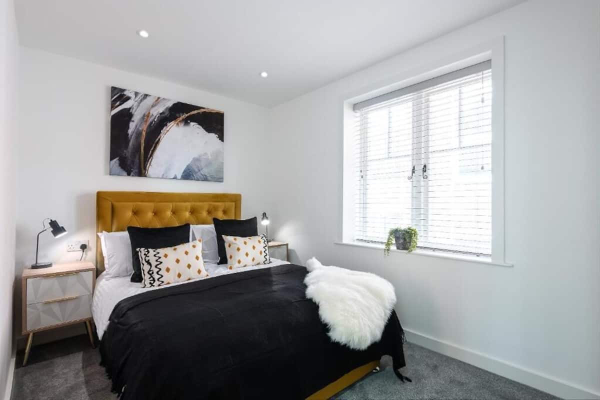 A bedroom with a bed, a nightstand, a window with blinds, and a painting on the wall.