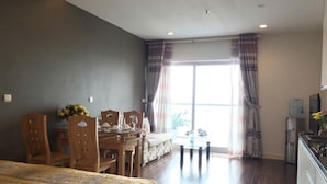 A room with a bed, a dining table with chairs, a small kitchen area, and a large window with curtains. - City Centre Apartment - Lancaster Hanoi (Hanoi)