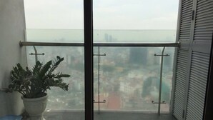 A balcony with a potted plant, a view of a cityscape, and a closed shutter door. - City Centre Apartment - Lancaster Hanoi (Hanoi)