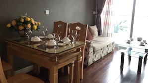 A dining area with a glass table, wooden chairs, and a sofa with a patterned cushion. - City Centre Apartment - Lancaster Hanoi (Hanoi)