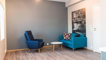 Et værelse med en blå lænestol, en blå sofa, et rundt sofabord og et maleri på væggen.
