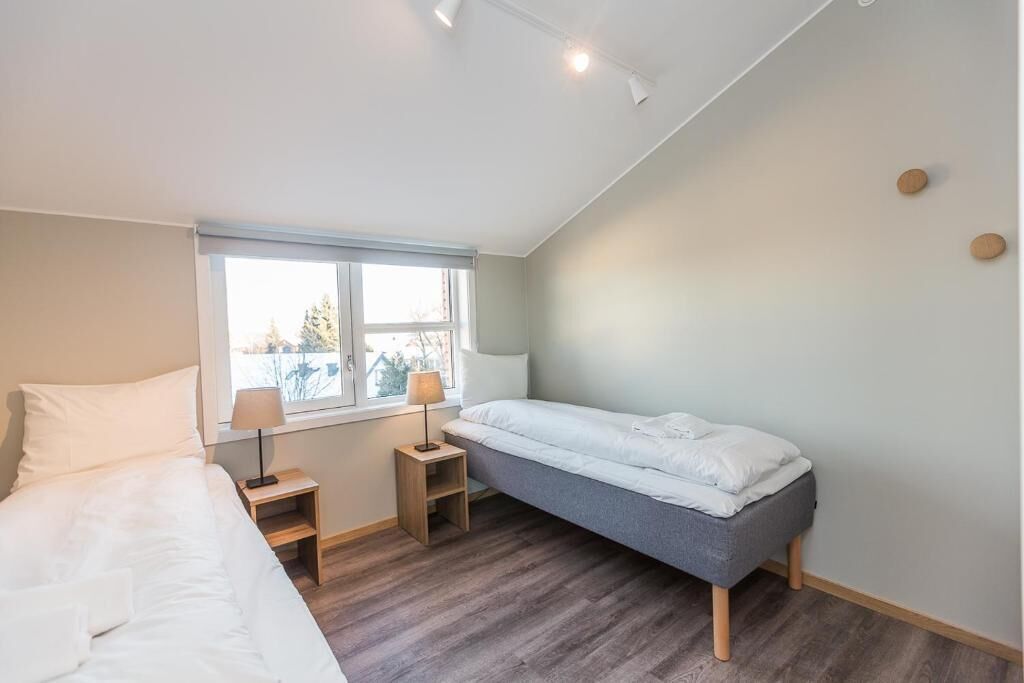 A bedroom with a bed, a desk, a chair, a window, and a bedside table.