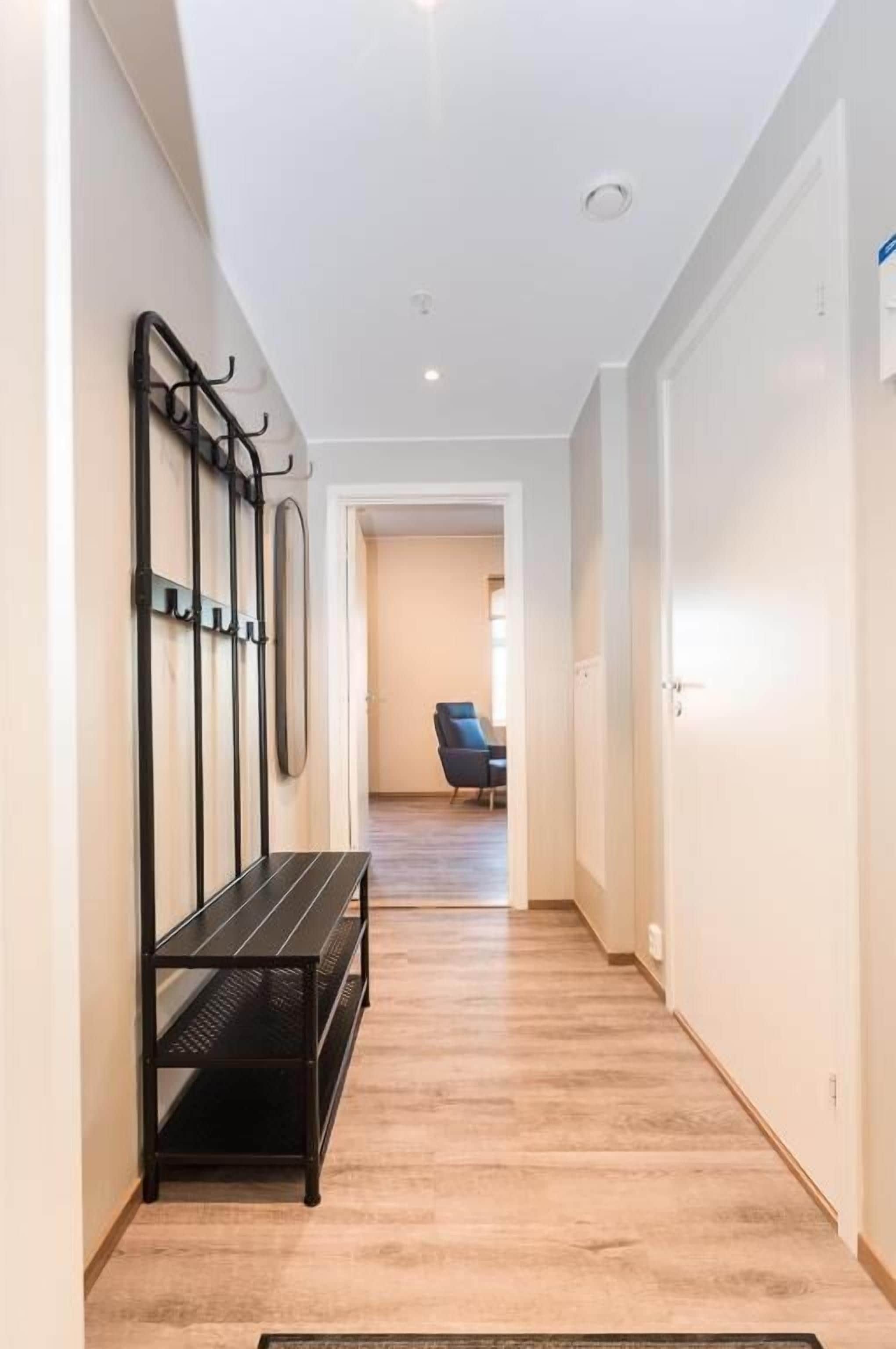 Un pasillo con un banco, ganchos en la pared y una puerta que da a una habitación con una silla.