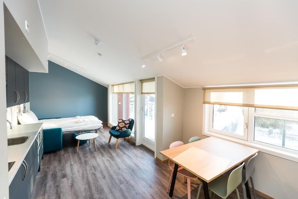 A modern room with a bed, a dining table, a chair, and a window.