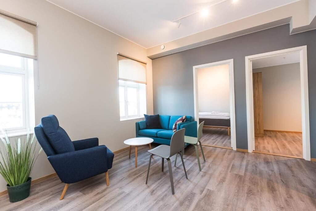 A modern living room with a blue sofa, a blue armchair, a small round table, and a potted plant.
