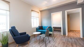 A modern living room with a blue sofa, a blue armchair, a small round table, and a potted plant.