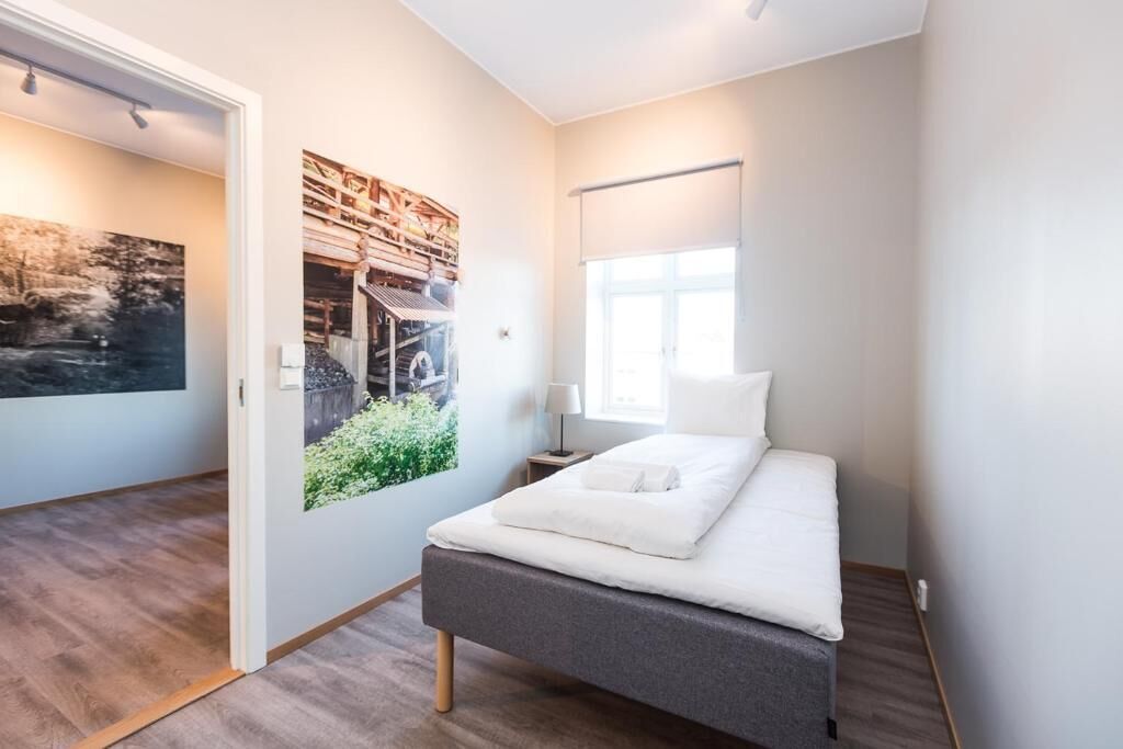 Een slaapkamer met een bed, een nachtkastje, een wandlamp, een raam en een ingelijste foto.