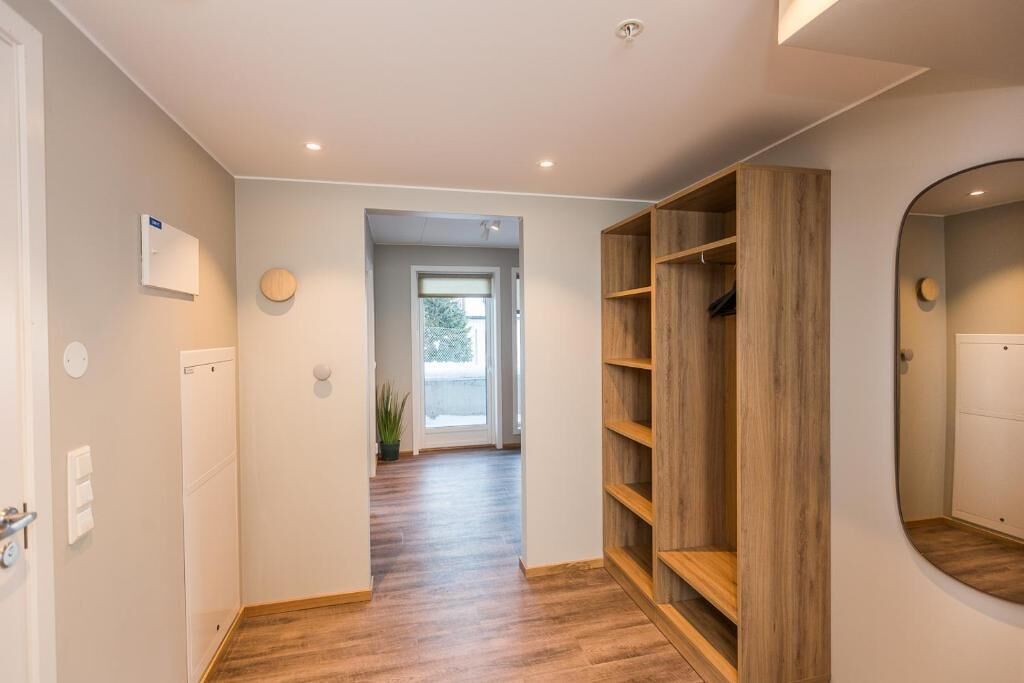 Un pasillo con piso de madera, un armario empotrado de madera, un espejo redondo y una puerta que conduce a otra habitación.
