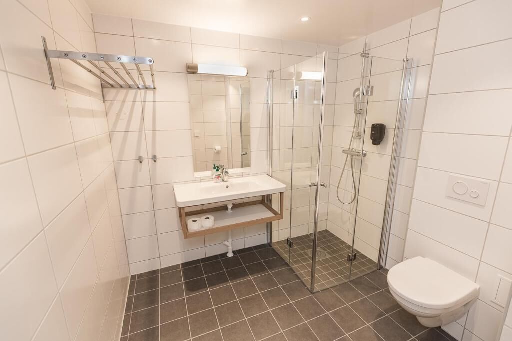 Une salle de bain moderne avec une douche à parois de verre, un lavabo blanc avec un miroir au-dessus et des toilettes.