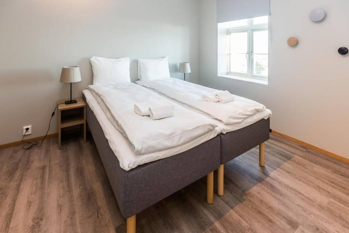 Quarto moderno com cama de casal, mesas de cabeceira e uma janela.