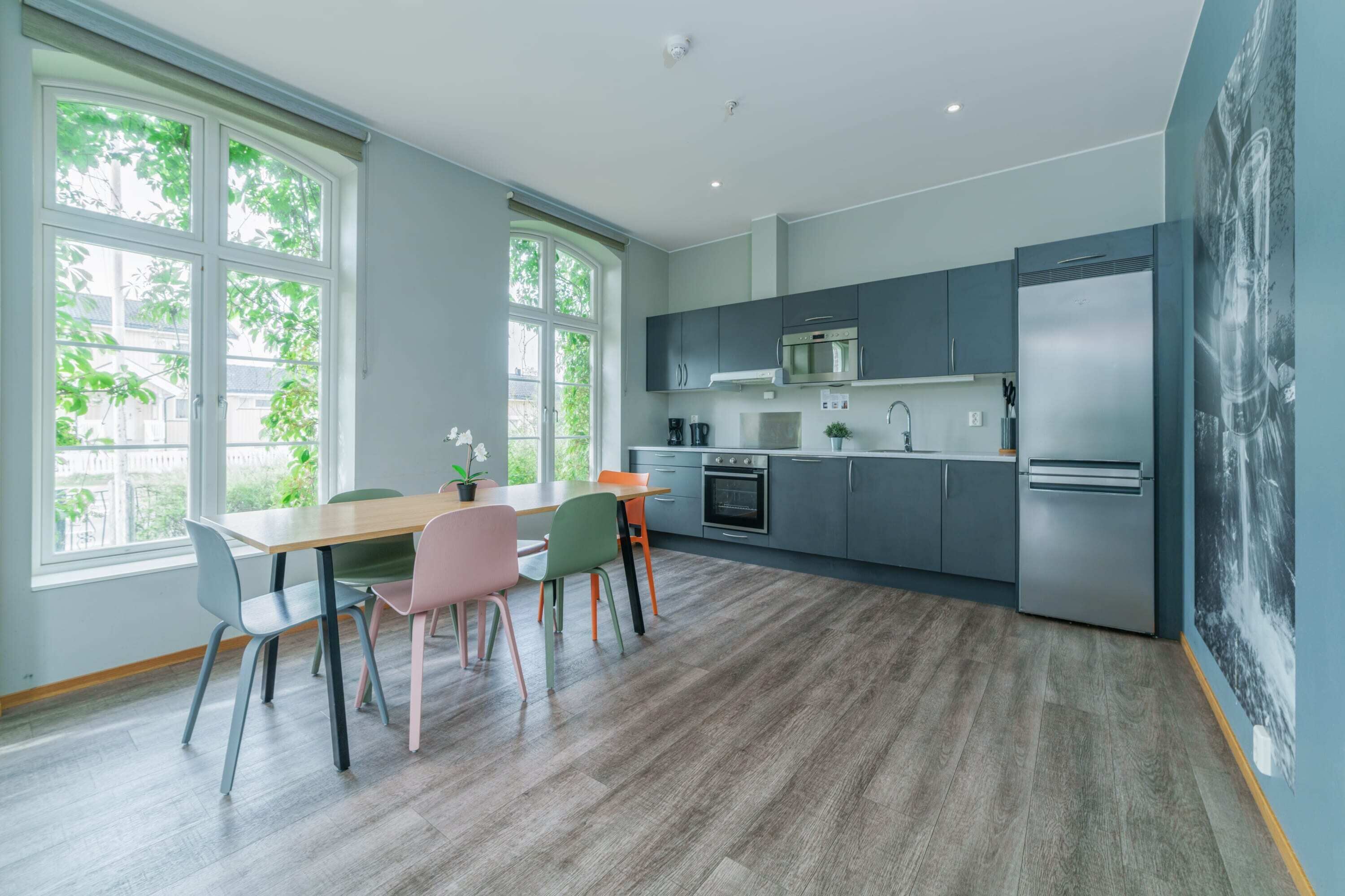 Eine moderne Küche mit grauen Schränken, einem Edelstahlkühlschrank und einem Essbereich mit Holztisch und bunten Stühlen.
