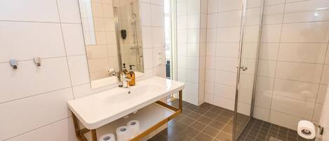 Un baño con lavamanos blanco, espejo y ducha.