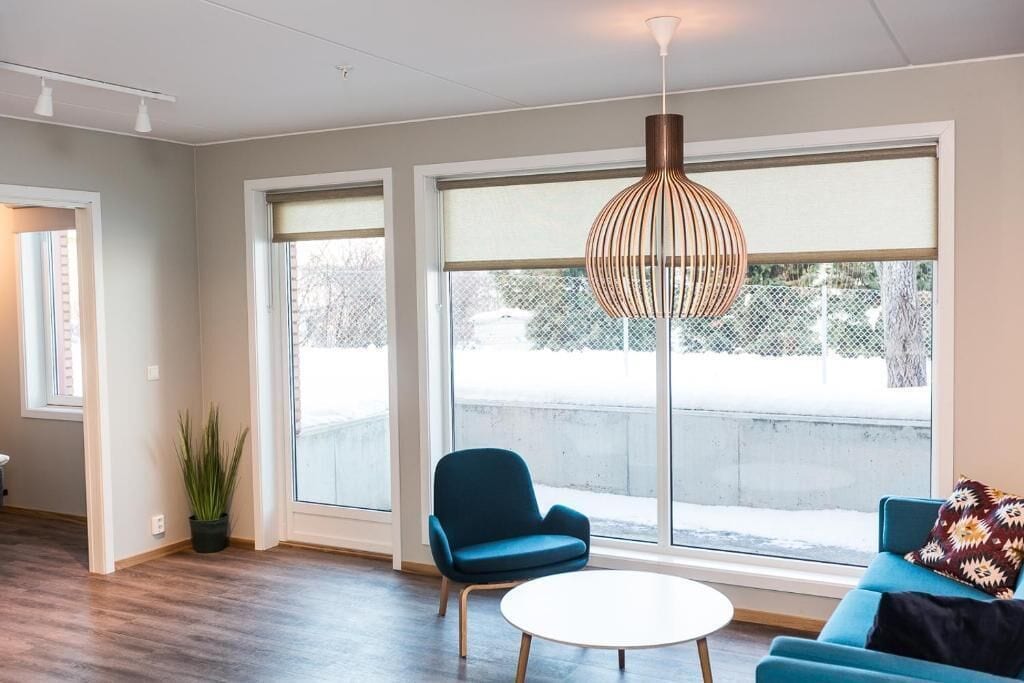 A room with large windows, a blue chair, a round table, and a hanging light fixture.