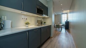 Una cocina moderna con armarios oscuros, un microondas y un lavamanos. Se ve un comedor con mesa y sillas al fondo.