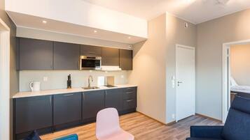 A compact living space with a kitchenette, a seating area with a blue sofa and a pink chair, and a door leading to another room.
