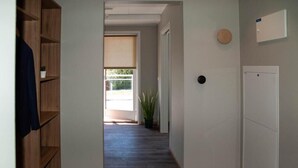 Un pasillo con una estantería de madera, una planta en maceta y una puerta que da a una habitación luminosa.